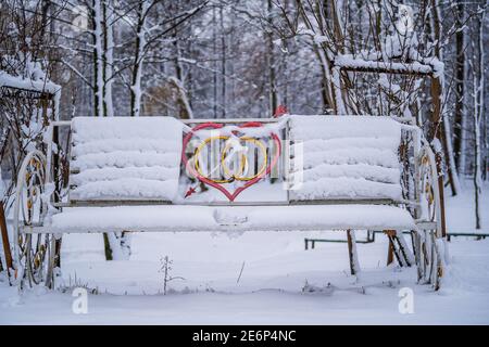 Banc décoratif avec coeur dans le parc d'hiver de la ville couvert de neige. Banc pour les amoureux en hiver, gros plan Banque D'Images