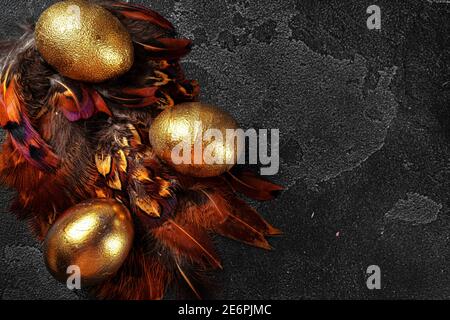 Œufs de Pâques dorés sur les plumes d'oiseau rouge gros plan Banque D'Images