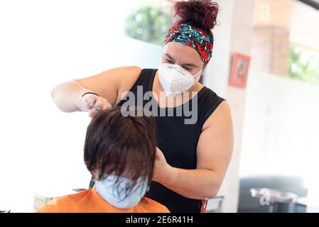 Travailler pendant le concept de covid-19 ou de coronavirus. Un coiffeur professionnel coupant les cheveux à un client avec un masque facial. Banque D'Images