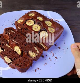 Placez à la main une assiette de chocolat noir maison frais Gâteau à la banane sur une table en bois Banque D'Images