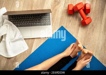 Femme sportive faisant du yoga fitness s'étirant à la maison via un ordinateur portable. Jeune femme perdant du poids par l'entraînement en ligne de gym en utilisant des haltères sur le plancher de la maison Banque D'Images