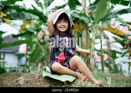 Jolie petite fille couvrant la tête avec livre après étude au jardin, éducation Nouveau concept normal Banque D'Images