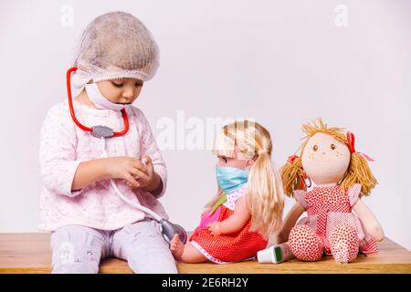 Une jeune fille joue un médecin d'enfant et traite des poupées sur un fond blanc. Banque D'Images