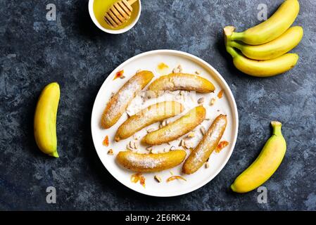 Bananes frites sur plaque blanche sur fond de pierre bleue. Dessert de bananes poêlées de style asiatique. Vue de dessus, plan d'appartement Banque D'Images