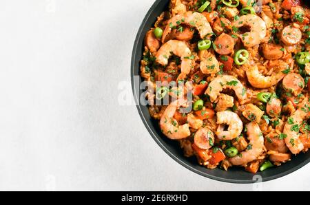 Vue rapprochée de jambalaya créole avec poulet, saucisses fumées et légumes dans une poêle sur fond de pierre blanche avec espace de copie. Vue de dessus, plate Banque D'Images