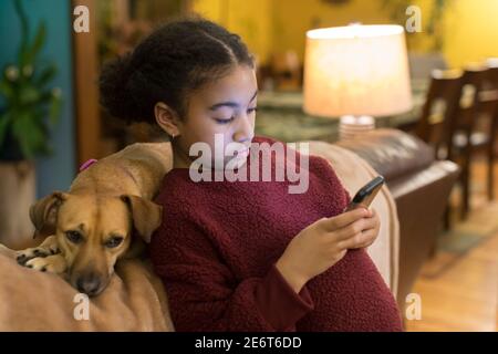 Tween biracial regardant le téléphone tout en se penchant contre le petit marron chien Banque D'Images