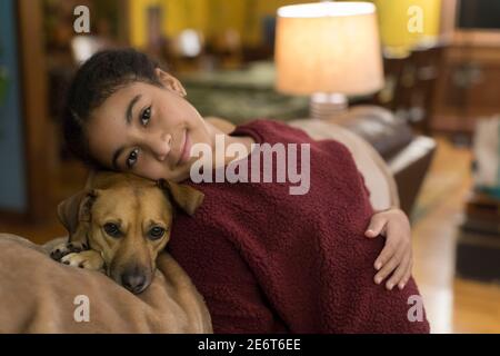 Tween biracial regardant la caméra tout en se penchant contre le petit marron chien Banque D'Images