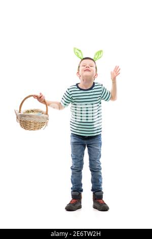 Jeune enfant excité avec des oreilles de lapin tenant le panier de Pâques regardant vers le haut avec la grimace de main levée. Pleine longueur isolée sur fond blanc. Banque D'Images