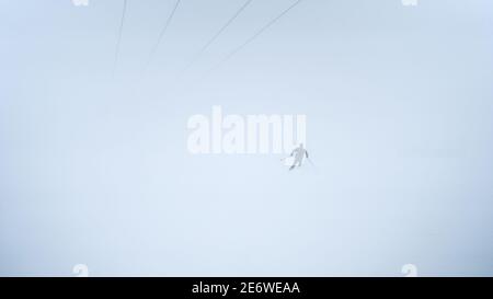 Les gens qui font du ski alpin pendant la tempête de neige. Les pistes de ski ont fermé le domaine skiable en raison du mauvais temps et du givrage. Homme athlète sur une pente enneigée par temps froid blanc Banque D'Images