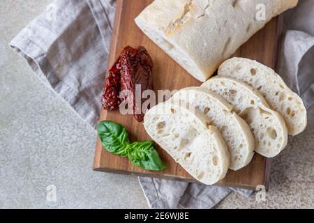 Pain ciabatta fraîchement cuit sur une assiette en bois avec tomates séchées et basilic, fond en béton. Mise au point sélective. Banque D'Images