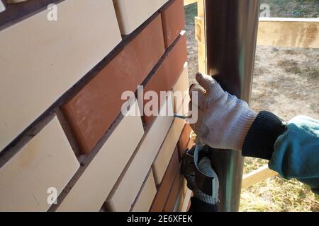 À la maison bricolée avec une brique avant, le travailleur fixe les tuyaux pour le drainage. La photo montre le mur, les tuyaux bruns et les mains du travailleur 2020. Banque D'Images