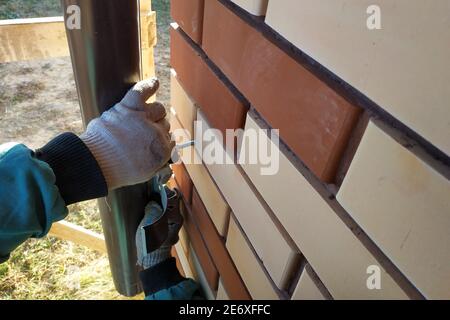 À la maison bricolée avec une brique avant, le travailleur fixe les tuyaux pour le drainage. La photo montre le mur, les tuyaux bruns et les mains du travailleur 2020. Banque D'Images