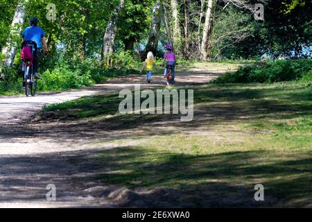 Parents et enfants à vélo dans le parc pendant l'heure autorisée pour l'exercice pendant le confinement - Reading, Berkshire, Angleterre, Royaume-Uni Banque D'Images