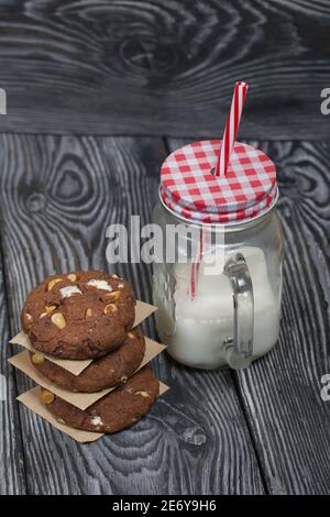 Biscuits aux flocons d'avoine avec arachides et chocolat. Plié dans une colonne et disposé avec du papier. Lait à proximité. Sur les planches de pin. Banque D'Images