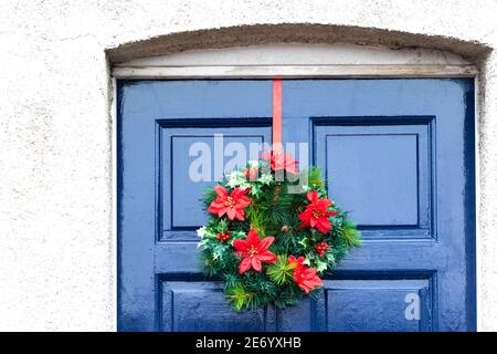 Des éléments en plastique dominent dans cette couronne de Noël accrochée à un porte avant en bois bleu Banque D'Images