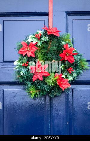 Des éléments en plastique dominent dans cette couronne de Noël accrochée à un porte avant en bois bleu Banque D'Images