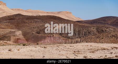 colline de basalte avec prismes dans le processus de décomposition dans les sols argileux rouges et roses avec le bord nord du cratère de maktesh ramon en israël Banque D'Images