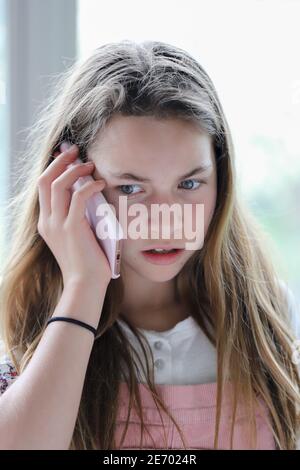 Jeune expressif belle brune preteen avec les cheveux longs et brun les yeux parlent sur un téléphone portable avec un étui rose exprimant un look de incrédulité et de doute Banque D'Images