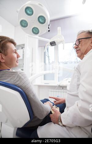 Photo verticale à angle bas d'un homme qui parle à lui dentiste expérimenté au cabinet dentaire Banque D'Images