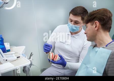 Dentiste masculin éduquant son patient, expliquant l'hygiène dentaire sur un modèle dentaire, espace de copie Banque D'Images