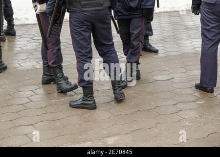 Les officiers de police russes se présentent sous la forme de bottines noires, d'un pantalon à rayures rouges et de bâtons de nuit en caoutchouc tonfa sur une surface mouillée - gros plan avec sélecteur Banque D'Images