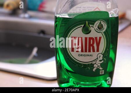 Une bouteille de liquide vaisselle devant un évier de cuisine rempli de vaisselle Banque D'Images