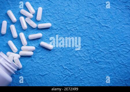 Vue de dessus des comprimés médicaux blancs dispersés sur la surface bleue Banque D'Images