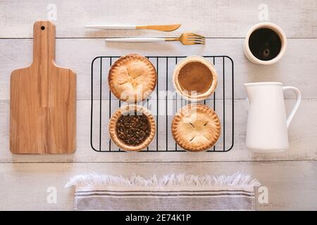 Quatre mini-chaussons directement du four sur une table en bois blanc avec un pot à lait, planche à découper Banque D'Images