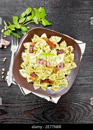 Pâtes Farfalle à la sauce pesto, bacon frit et basilic dans une assiette sur une serviette sur fond de bois d'en haut Banque D'Images