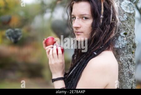 Belle jeune personne, femme excentrique, avec des dreadlocks attrayants, piercing et tatouage montrant dans le jardin d'Eden appelant à la pomme de te Banque D'Images