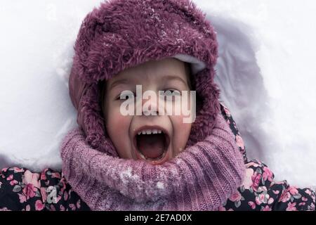 Concepts d'hiver, de famille, d'enfance - portrait en gros plan petite fille authentique d'âge préscolaire en vêtements roses sourire rire crier avec la bouche ouverte sur Banque D'Images