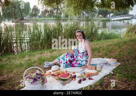 Une jeune femme est assise sur un pique-nique dans un parc sur les rives d'une rivière Banque D'Images
