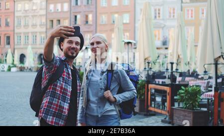Couple de touristes faisant selfie sur smartphone dans le centre-ville. Ils ont des sacs de touristes. Banque D'Images