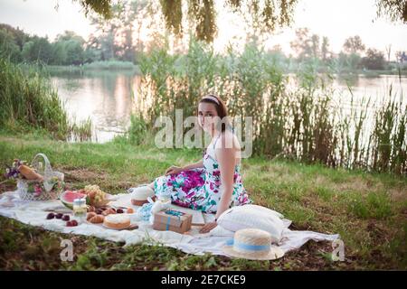 Une jeune femme est assise sur un pique-nique dans un parc sur les rives d'une rivière Banque D'Images