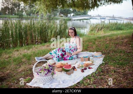Une jeune femme est assise sur un pique-nique dans un parc sur les rives d'une rivière Banque D'Images