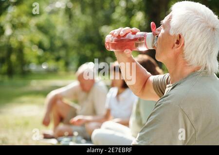 Homme senior qui boit de l'eau à la bouteille après un entraînement sportif dans le parc à l'extérieur Banque D'Images