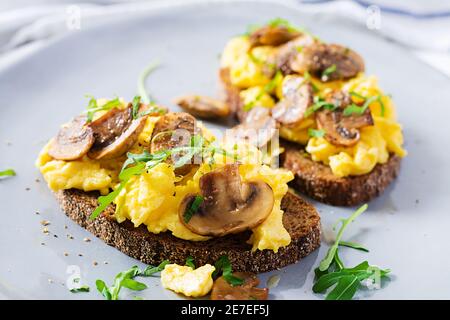 Œufs brouillés et champignons frits sur le pain. Petit-déjeuner ou brunch fait maison - œufs brouillés et sandwichs aux champignons. Banque D'Images