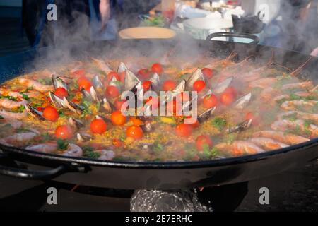 Paella cuite avec crevettes, muse, riz, tomates cerises dans une grande casserole - gros plan Banque D'Images