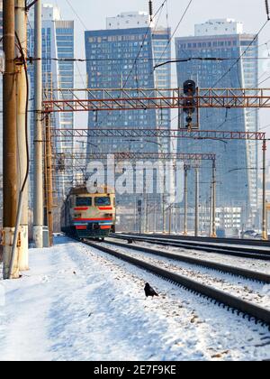 Un train électrique se déplace sur des rails sur fond de paysage urbain, dans une image verticale de brume hivernale. Banque D'Images