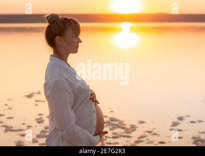 Portrait d'une jolie jeune femme enceinte sur une plage. Une femme se repose et se détend au coucher du soleil Banque D'Images