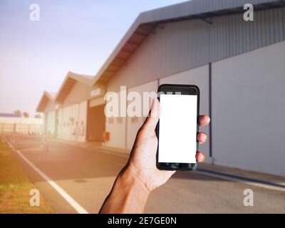 Main d'œuvre tenant un smartphone noir avec écran vide derrière un bâtiment industriel avec un arrière-plan flou. Espace pour le texte ou la conception Banque D'Images