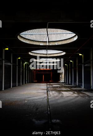 Garage souterrain en béton sombre de mauvaise humeur, garage en créepy, évents circulaires sur le toit les rayons de lumière du jour qui brillent créent un univers industriel futuriste moody Banque D'Images