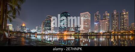 Un banc près du lac dans le parc Benjakiti avec des gratte-ciels la nuit à Bangkok, Thaïlande Banque D'Images