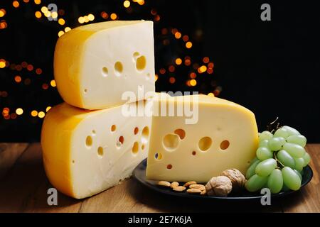 Fromage sur table avec raisins et noix. Tête de fromage dure moyenne edam, gouda, parmesan sur bois. Concept de saine alimentation. Banque D'Images