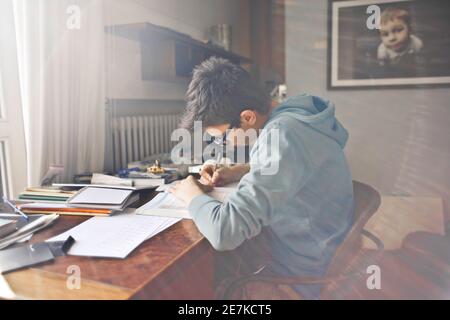 Garçon à lunettes et pull à capuche gris faisant ses devoirs sa chambre Banque D'Images