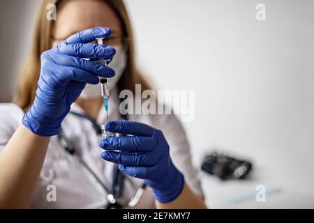 Une femme médecin portant un masque médical tire le vaccin du coronavirus dans une seringue à la clinique.le concept de vaccination, d'immunisation, de prévention Banque D'Images