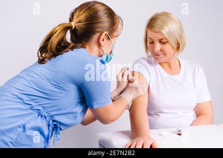 Un médecin en uniforme médical bleu met le vaccin avec une seringue à une femme blonde âgée. Arrière-plan blanc. Banque D'Images