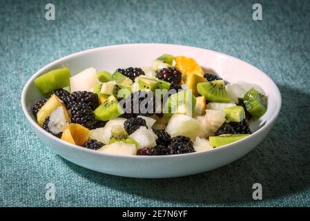 Un bol de salade de fruits avec des mûres, des kiwis, du melon et de l'orange. Banque D'Images