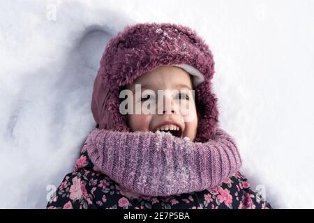 Concepts d'hiver, de famille, d'enfance - portrait en gros plan petite fille authentique d'âge préscolaire en vêtements roses sourire rire crier avec la bouche ouverte sur Banque D'Images