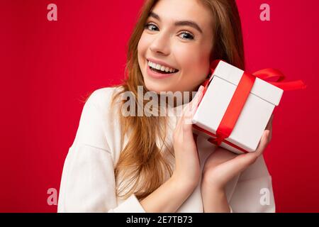 portrait en gros plan photo de jeune blond charmant et souriant femme isolée sur fond rouge mur portant décontracté blanc sweat à capuche maintien Banque D'Images